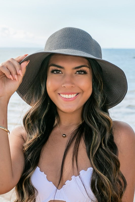 A person holding onto a Bow Back Straw Bucket Hat at the beach.