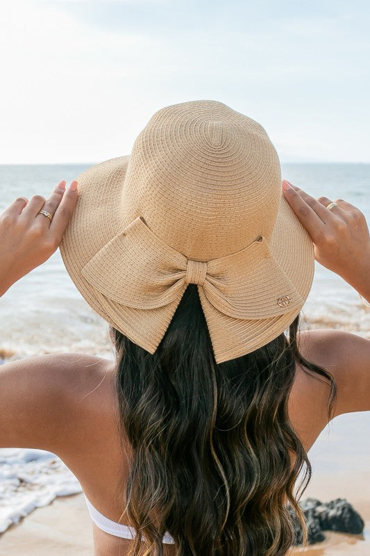 A person holding onto a Bow Back Straw Bucket Hat at the beach.