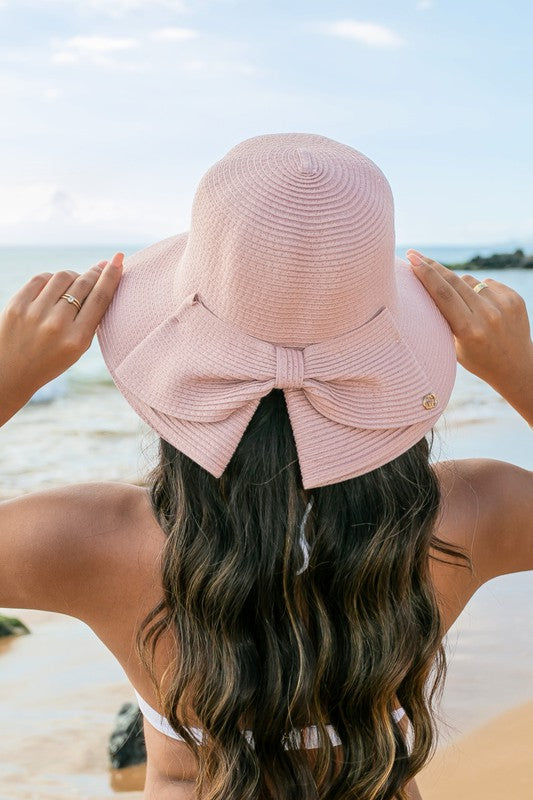 A person holding onto a Bow Back Straw Bucket Hat at the beach.