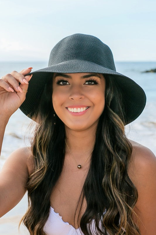 A person holding onto a Bow Back Straw Bucket Hat at the beach.