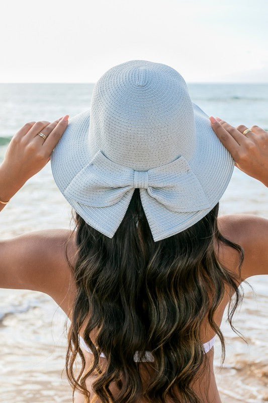 A person holding onto a Bow Back Straw Bucket Hat at the beach.