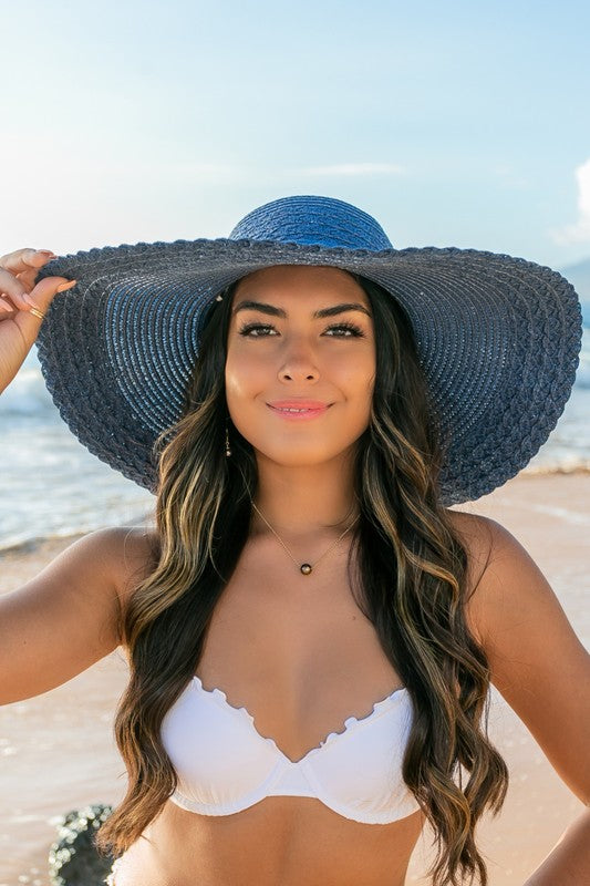 A woman holding her Scallop Edge Bow Accent Sunhat while standing on a beach.