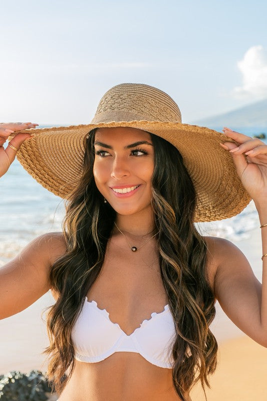A woman holding her Scallop Edge Bow Accent Sunhat while standing on a beach.