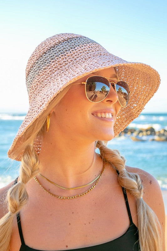Woman smiling with sunglasses and a Stripe Accent Straw Bucket Hat at the beach.