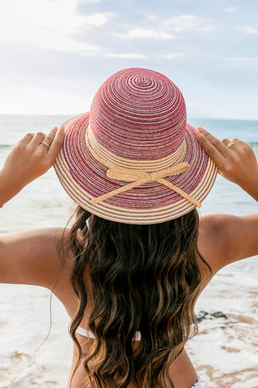 A person holding onto a Multi-Stripe Bow Accent Bucket Sunhat while facing the sea.