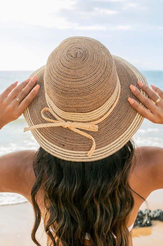 A person holding onto a Multi-Stripe Bow Accent Bucket Sunhat while facing the sea.