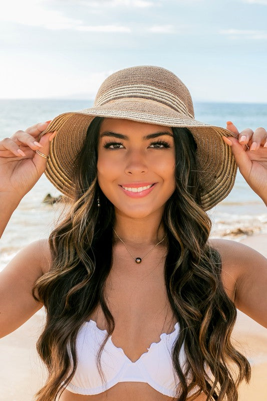 A person holding onto a Multi-Stripe Bow Accent Bucket Sunhat while facing the sea.