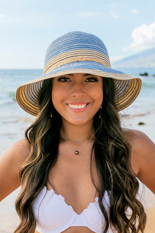 A person holding onto a Multi-Stripe Bow Accent Bucket Sunhat while facing the sea.