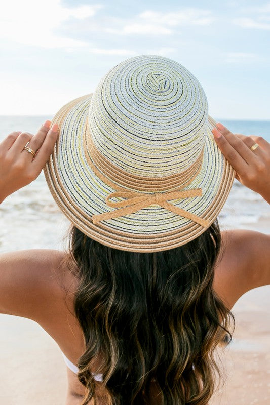 A person holding onto a Multi-Stripe Bow Accent Bucket Sunhat while facing the sea.