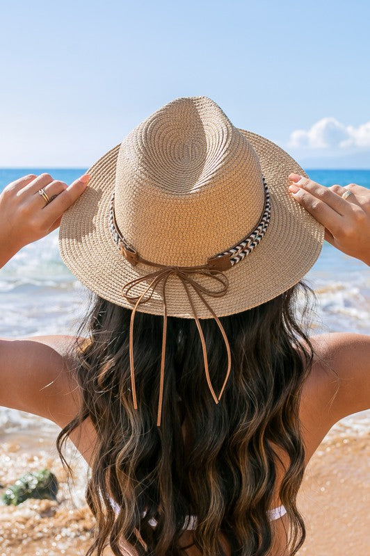 A woman holding the brim of her Boho Accent Straw Panama Fedora Hat on a sunny beach.