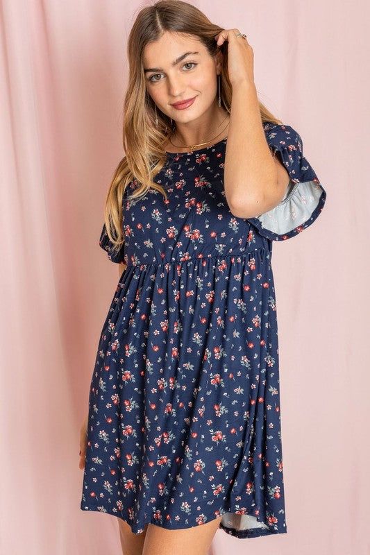 A person wearing the Plus Ditsy Floral Ruffle Chest Pocket Dress stands elegantly against a pink curtain backdrop.