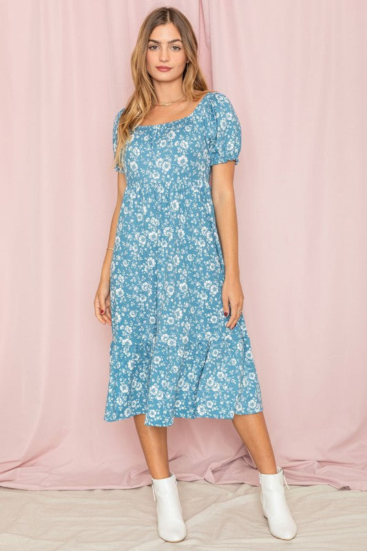 A woman wearing a Floral Square Neck Puff Sleeve Boho Dress stands in front of a pink curtain, looking to the side.