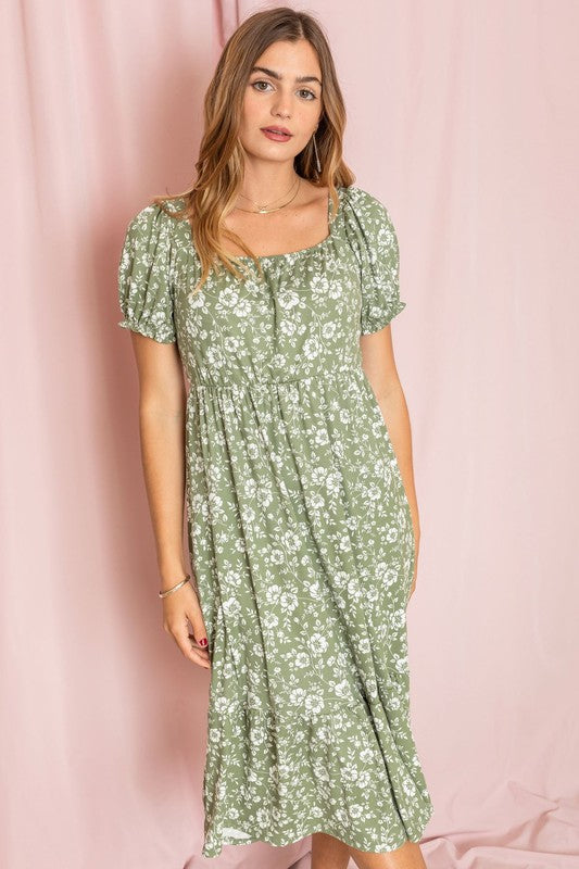 A woman wearing a Floral Square Neck Puff Sleeve Boho Dress stands in front of a pink curtain, looking to the side.