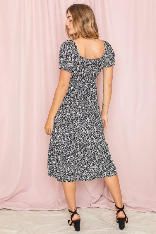 A woman wearing a Floral Square Neck Puff Sleeve Boho Dress stands in front of a pink curtain, looking to the side.