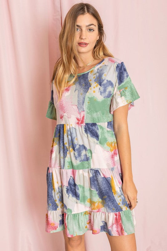 A person wearing a vibrant tie-dye ruffle midi dress and white ankle boots stands in front of a pink backdrop.