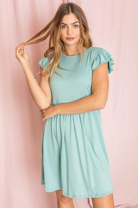 A woman wearing the Plus Solid Ruffle Cap Sleeve Midi Dress stands against a pink backdrop, looking down and gently holding her hair.