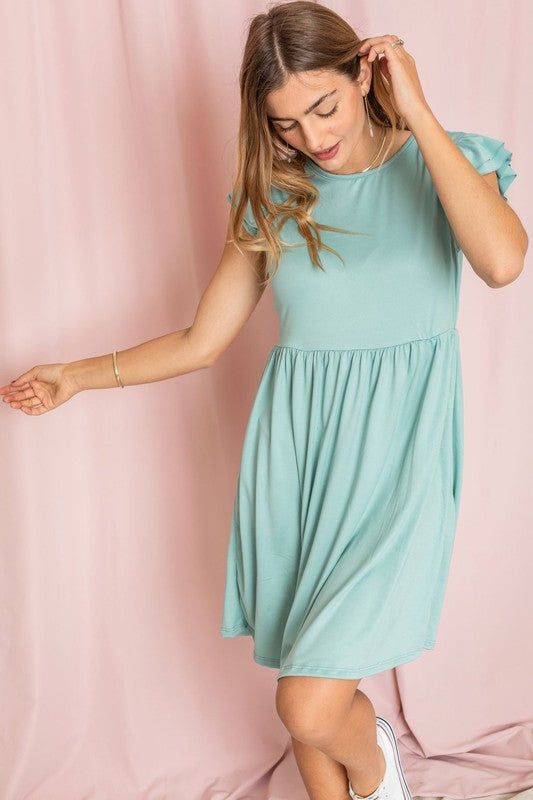 A woman wearing the Plus Solid Ruffle Cap Sleeve Midi Dress stands against a pink backdrop, looking down and gently holding her hair.