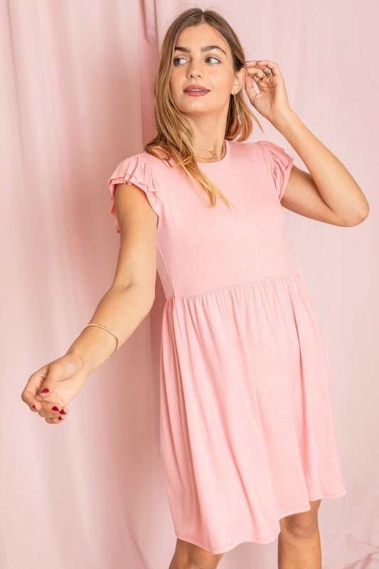 A woman wearing the Plus Solid Ruffle Cap Sleeve Midi Dress stands against a pink backdrop, looking down and gently holding her hair.