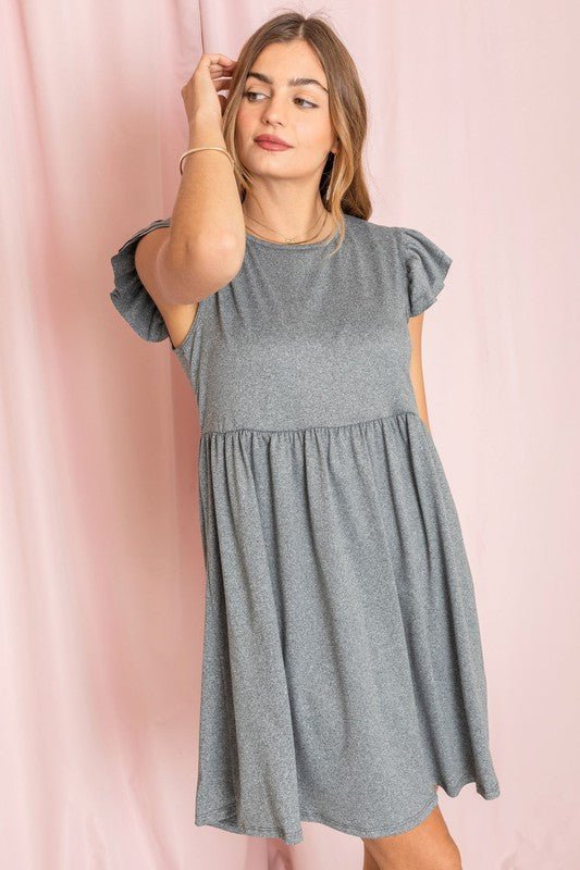 A woman wearing the Plus Solid Ruffle Cap Sleeve Midi Dress stands against a pink backdrop, looking down and gently holding her hair.