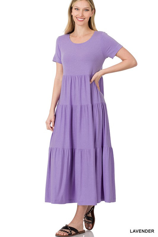 A person is wearing the versatile Short Sleeve Tiered Midi Dress in lavender paired with black sandals, positioned against a white backdrop.