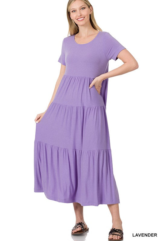 A person is wearing the versatile Short Sleeve Tiered Midi Dress in lavender paired with black sandals, positioned against a white backdrop.