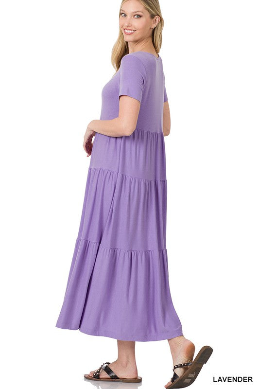 A person is wearing the versatile Short Sleeve Tiered Midi Dress in lavender paired with black sandals, positioned against a white backdrop.