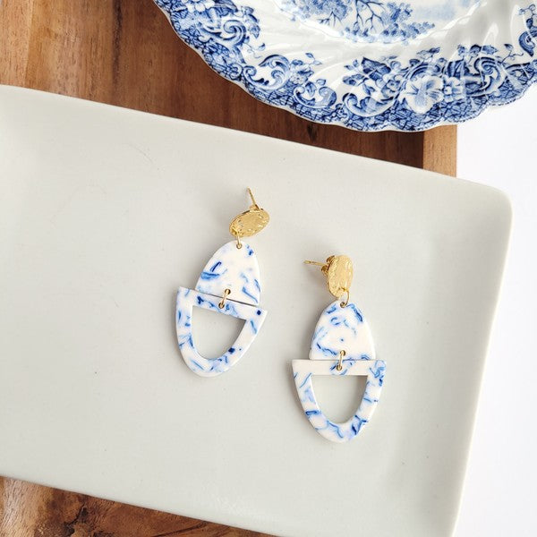 Athena Greek Goddess collection features stunning white and blue marbled earrings with gold accents, elegantly arranged on a hexagonal plate set on a wooden tray. These earrings are crafted with hypoallergenic stainless steel, perfect for sensitive ears.