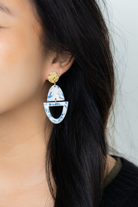 Athena Greek Goddess collection features stunning white and blue marbled earrings with gold accents, elegantly arranged on a hexagonal plate set on a wooden tray. These earrings are crafted with hypoallergenic stainless steel, perfect for sensitive ears.