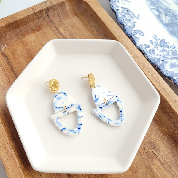 Athena Greek Goddess collection features stunning white and blue marbled earrings with gold accents, elegantly arranged on a hexagonal plate set on a wooden tray. These earrings are crafted with hypoallergenic stainless steel, perfect for sensitive ears.