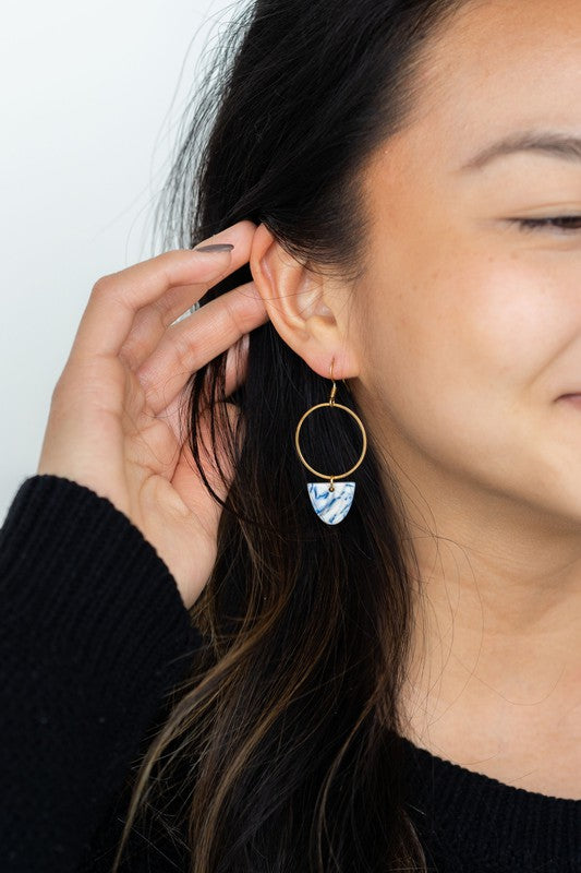 From the Greek Goddess collection, the Iris Earrings - Greek Goddess Blue feature gold hoops and heart-shaped blue and white pendants, elegantly displayed on a hexagonal white dish atop a wooden surface. Made from hypoallergenic stainless steel, they combine both style and comfort seamlessly.