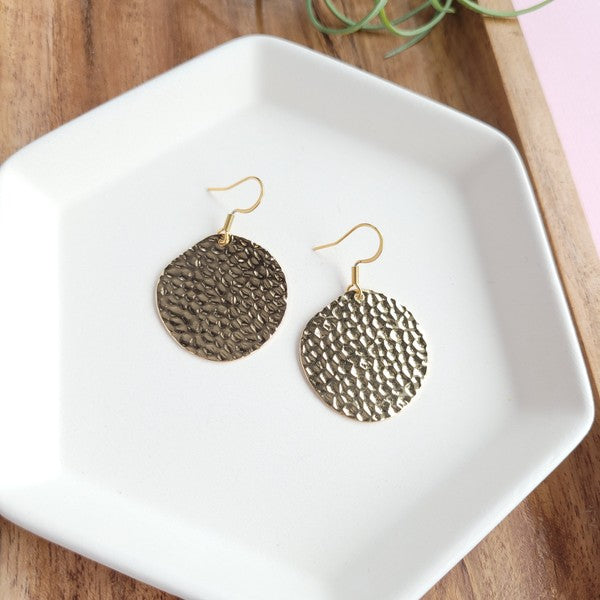 Wearing a black sweater, a person with a cheerful smile adjusts their hair while showcasing the Lucia Earrings - Gold.