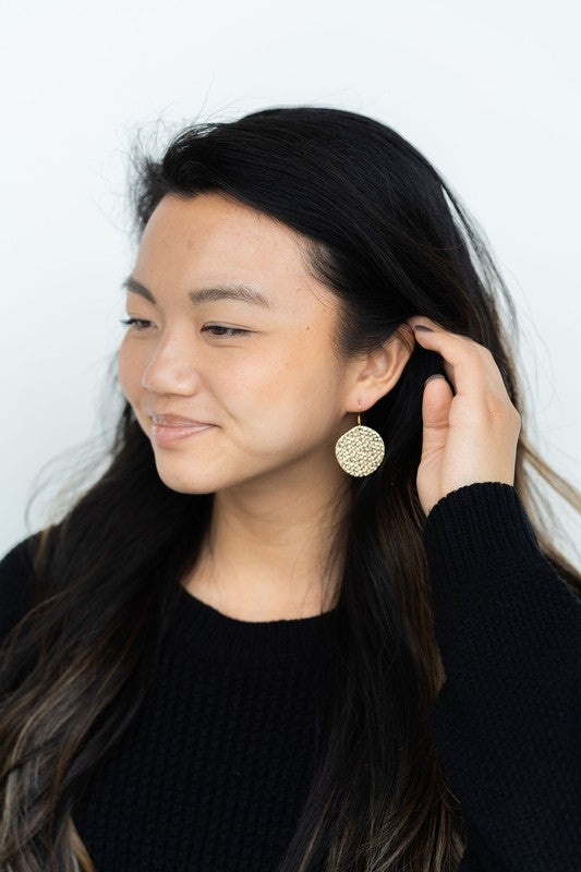 Wearing a black sweater, a person with a cheerful smile adjusts their hair while showcasing the Lucia Earrings - Gold.