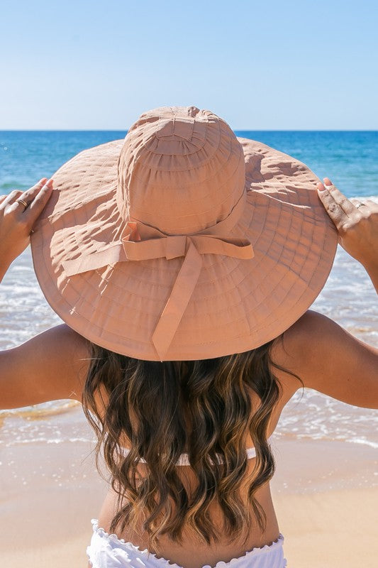 Woman holding a Classic Bow Accent Sunhat Extra Wide Brim at the beach.
