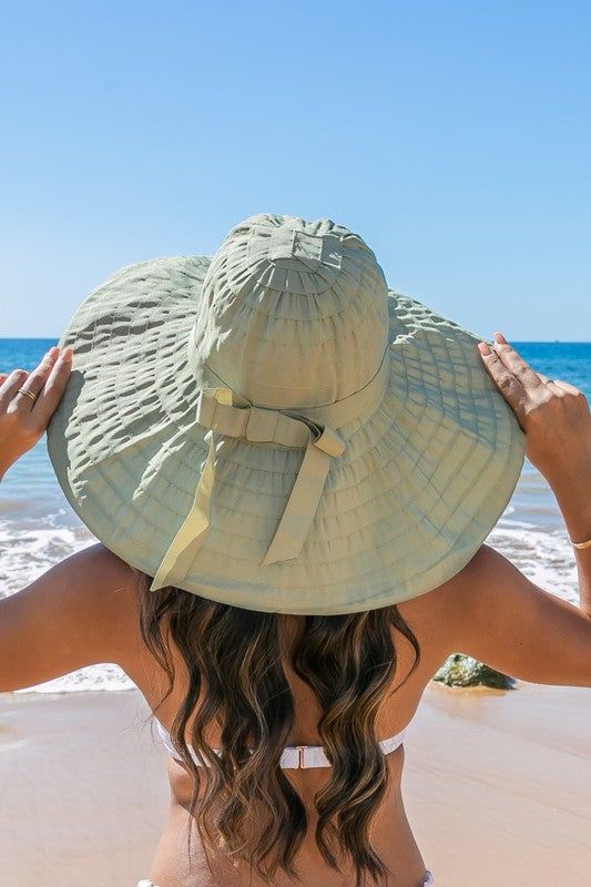 Woman holding a Classic Bow Accent Sunhat Extra Wide Brim at the beach.