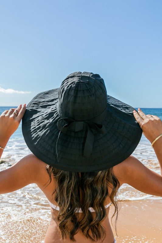Woman holding a Classic Bow Accent Sunhat Extra Wide Brim at the beach.