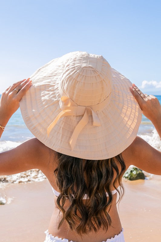 Woman holding a Classic Bow Accent Sunhat Extra Wide Brim at the beach.