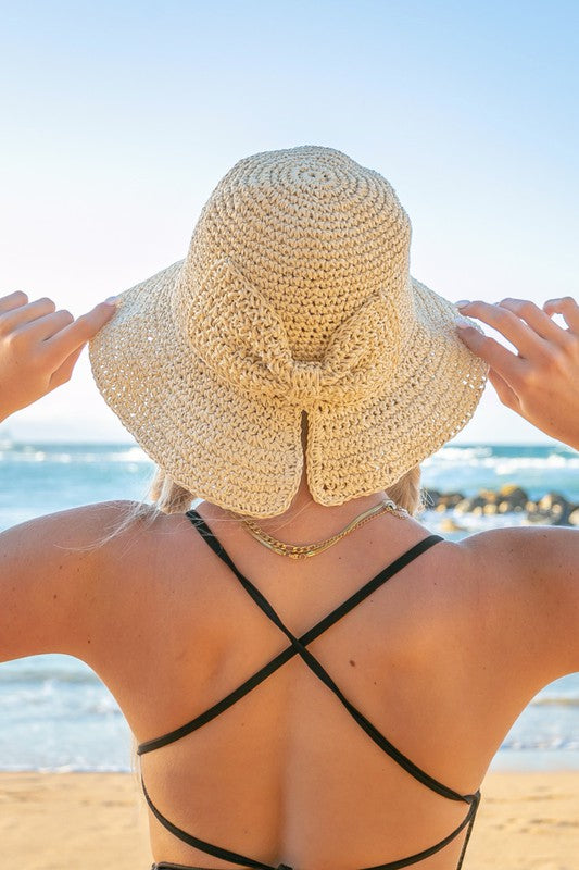 Woman holding a Bow Accent Woven Straw Bucket Sun Hat at the beach, facing away from the camera.