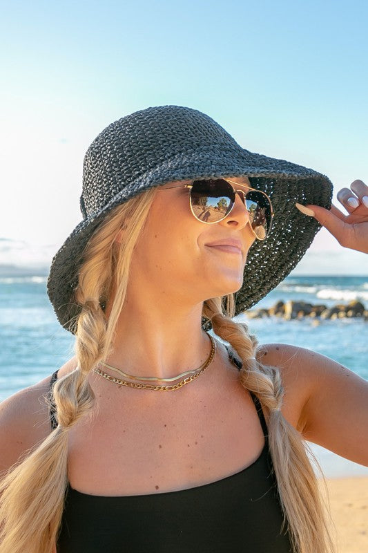 Woman holding a Bow Accent Woven Straw Bucket Sun Hat at the beach, facing away from the camera.