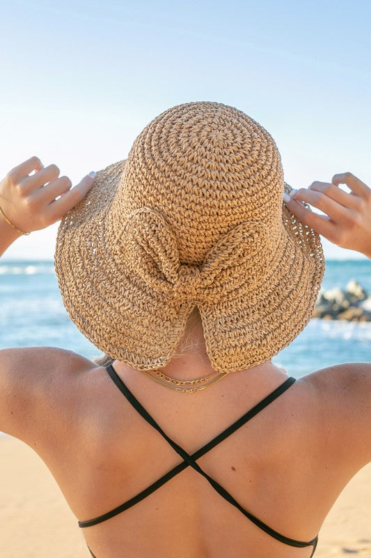Woman holding a Bow Accent Woven Straw Bucket Sun Hat at the beach, facing away from the camera.