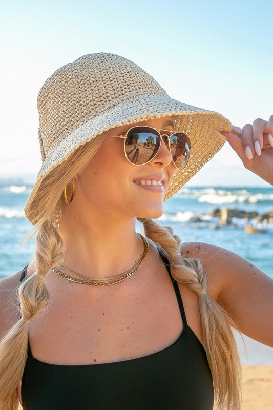 Woman holding a Bow Accent Woven Straw Bucket Sun Hat at the beach, facing away from the camera.