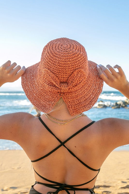 Woman holding a Bow Accent Woven Straw Bucket Sun Hat at the beach, facing away from the camera.