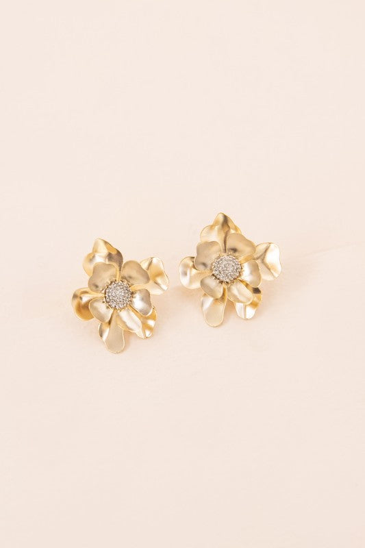 Anemone Post Earrings showcase flower-shaped designs with textured centers and gleaming gold petals, beautifully set against a light beige backdrop.