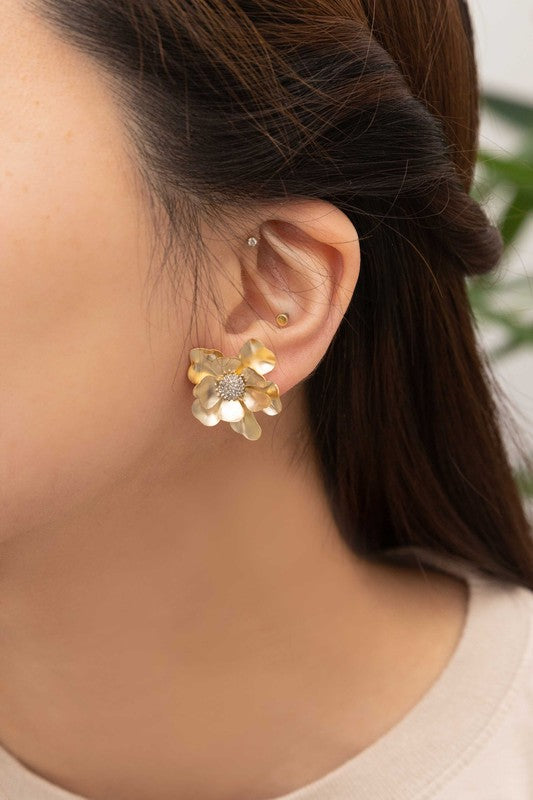 Anemone Post Earrings showcase flower-shaped designs with textured centers and gleaming gold petals, beautifully set against a light beige backdrop.