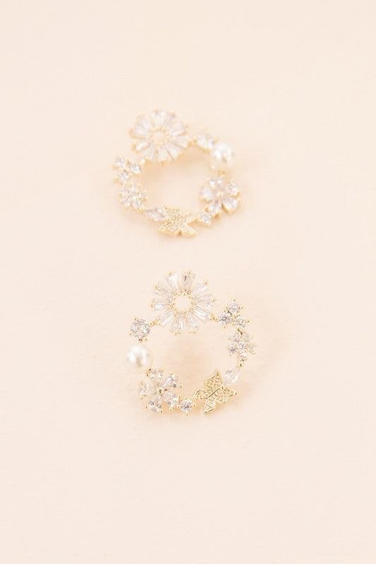 Fable Post Earrings showcase a circular arrangement of gold floral designs and pearl accents, all set against a beige background with a touch of subtle gold plating to enhance their elegance.