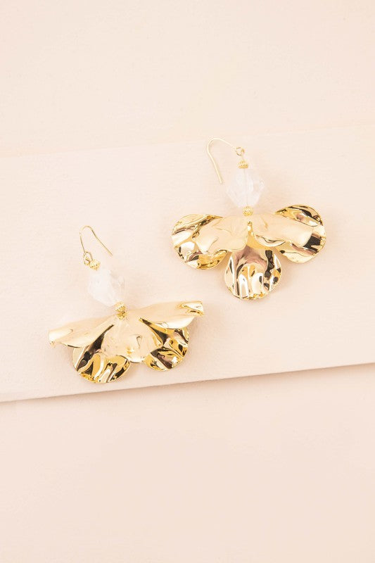 Snowdrop Hook Earrings: These elegant earrings showcase white, petal-shaped drops complemented by hooks with 10k gold plating, all beautifully presented on a beige background.