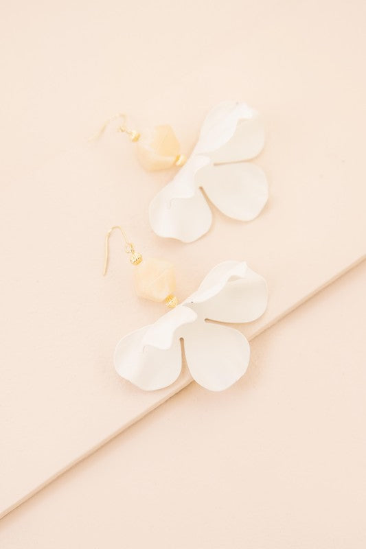 Snowdrop Hook Earrings: These elegant earrings showcase white, petal-shaped drops complemented by hooks with 10k gold plating, all beautifully presented on a beige background.