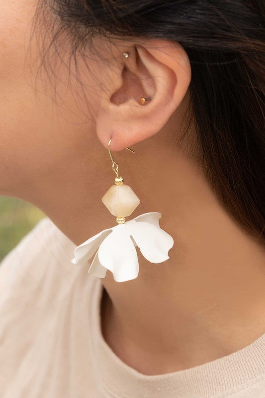 Snowdrop Hook Earrings: These elegant earrings showcase white, petal-shaped drops complemented by hooks with 10k gold plating, all beautifully presented on a beige background.