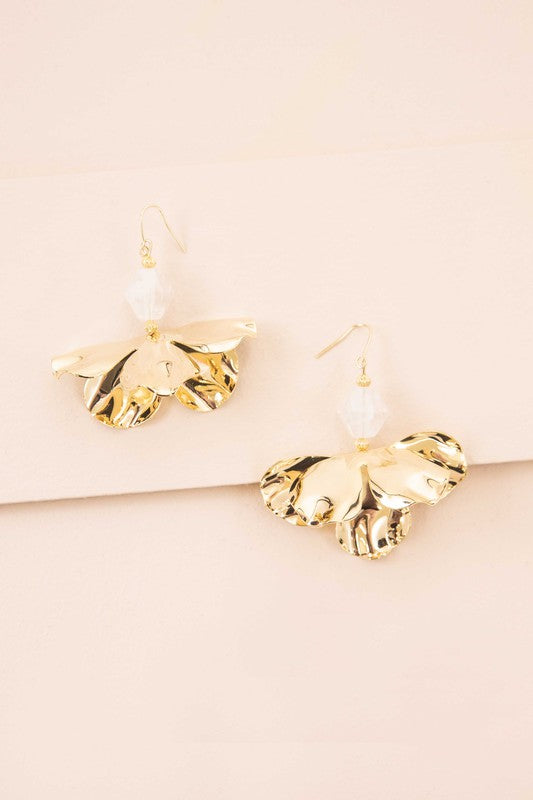 Snowdrop Hook Earrings: These elegant earrings showcase white, petal-shaped drops complemented by hooks with 10k gold plating, all beautifully presented on a beige background.