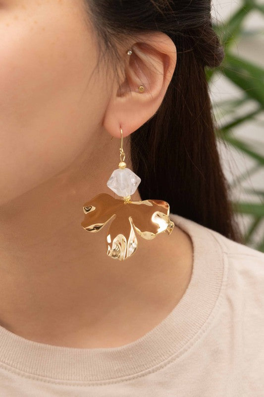 Snowdrop Hook Earrings: These elegant earrings showcase white, petal-shaped drops complemented by hooks with 10k gold plating, all beautifully presented on a beige background.