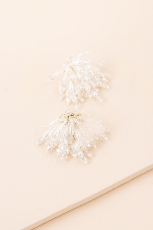 Introducing the Flare Drop Earrings—a pair of elegant white tassel earrings featuring intricate beaded details on a light background, perfect for completing a bridal ensemble. The sterling silver post adds an extra touch of sophistication.